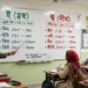 শিক্ষক ব্ল্যাকবোর্ডে ই ও ঈ দিয়ে শব্দের উচ্চারণরীতি শেখাচ্ছেন